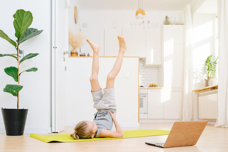 Cute little boy doing candle stands, next to a laptop. Physical athletic exercise on isolation at...