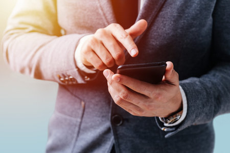 A man in a business suit holds a phone in his hand and puts his hand on the screen to press. Hands...