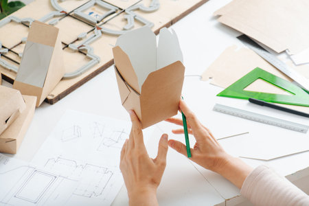 Box maker working behind a table in a private workshop, studying, looking at one, tools scattered...