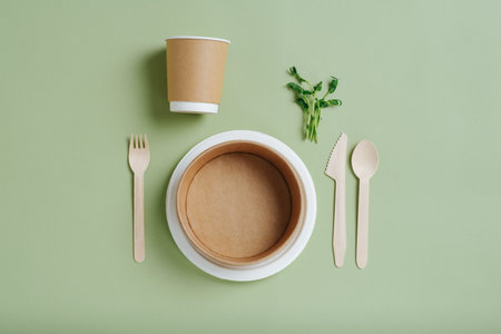Eco-friendly dinner set. Sugarcane and paper dishes, sugarcane cup in paper holder and bamboo utensils. Top view. Over green background. Disposable and compostable dishware. Pea plant next to them.の写真素材
