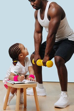 Staying in the mood for physical activity during  quarantine. Black father doing squats, his daughter taking notes.の写真素材