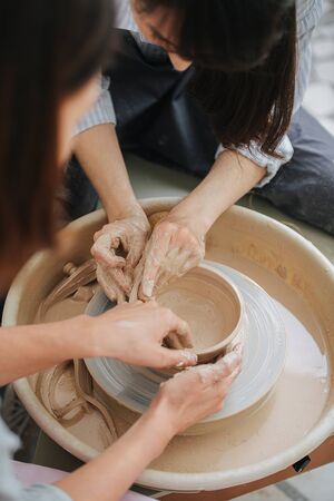 One woman teaching another how to shape bowl together on a pottery wheel in a private workshop. Chance to spent time on hobby during isolation.の写真素材