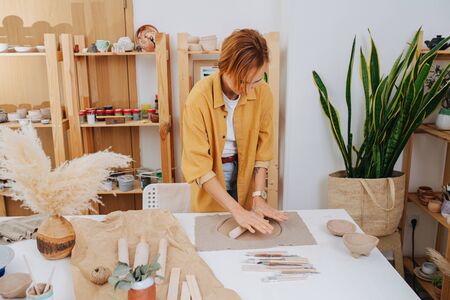 Redhead woman rolling clay circle in her private workshop. Chance to spent time on her hobby during isolation.の写真素材