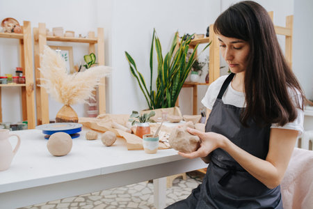 Brunette woman molding clay into shape in her private workshop. Chance to spent time on her hobby...