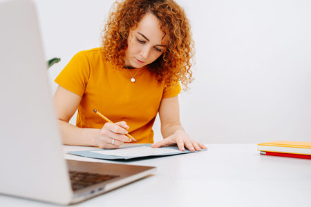 Focused artist woman drawing behind work desk in her notepad with a pencil