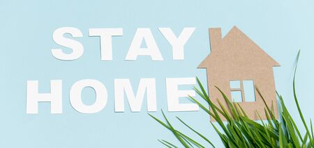 Cardboard stay home message laid on a blue surface along with house shape and natural grass under itの写真素材