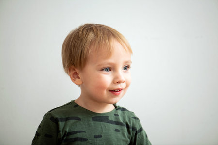 Funny blond toddler boy in green long-sleeve over white room wall