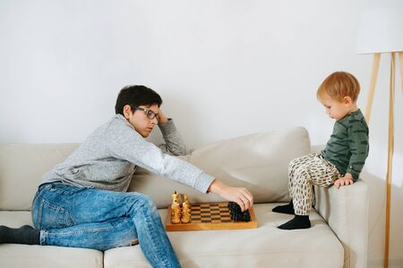 Father teaching his toddler son how to play chess on a sofa at home. They are lining up pieces. Learning how to place them properly.の写真素材