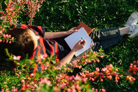Top view of girl, she sitting on grass in a flowered garden with a notepad and pen in her handsの写真素材