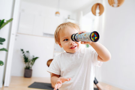 Fair little toddler boy looking into kaleidoscope. Blurred. Focus on a boy. At home