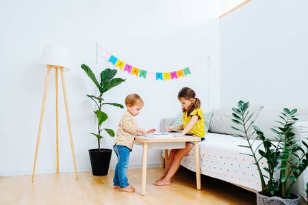 Little children drawing on a coffee table in a living room. Stay home flag garland hanging on the wall. Lonshotの写真素材