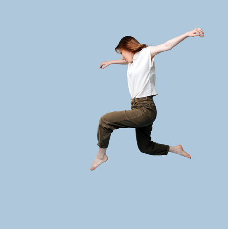 Young woman doing figure jump over blue background.