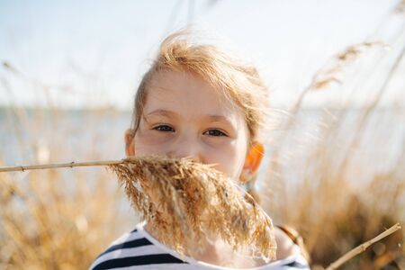 Portrait of a happy lively little six year old girl by the lake at spring, with dry grass all around. She's has cereal ear mustache.の写真素材