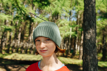 Portrait of a freckled ginger girl in a forest with feathers in her cap. Blurred surroundings.の写真素材