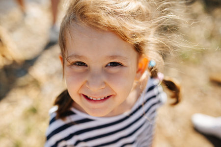 downward angle portrait of joyful little preschooler girl in a sunny day. Blurred dry grass...