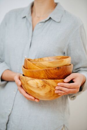 Cropped image of a woman in shirt holding stack of wooden bowls in her hands, she made them. No head.の写真素材