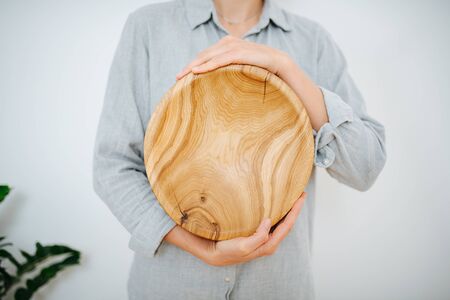 Cropped image of a woman vertically holding wooden bowl in her hands, she made it. Showing wood natural pattern. No head.の写真素材
