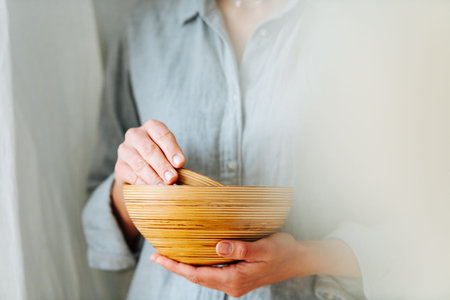 Woman holding wooden bowls in hands. Smaller one inside a bigger one. Cropped, no head. Fogged side.の写真素材