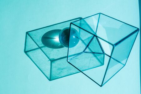 Glass cube, steel sphere and their disproportionate shadows, lit with blue light at a low angle. Abstrat composition. Cube standing on a corner, replaced with a triangle base.の写真素材