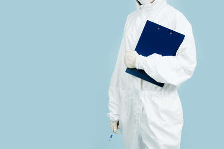 Fully geared up doctor in a white costume covering all skin and gloves holding plastic folder. Cropped, body and hips, no head.の写真素材