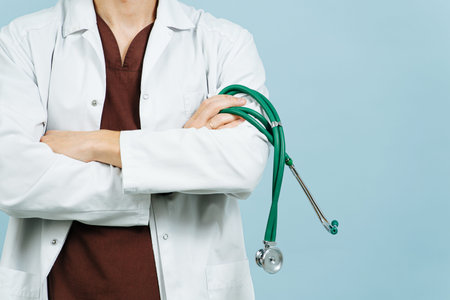 Cropped image of a male doctor in a white robe with hands crossed over blue