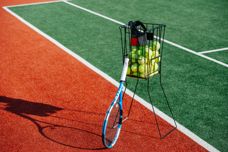 Tennis ball basket and a racket standing next to the line between inner part ond outer clearence...