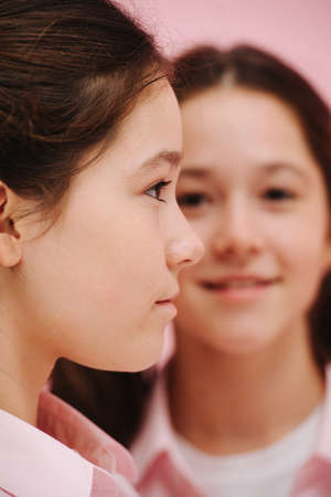 Beautiful little twin sisters posing. Over pink background, studio shot. One is facing right side, other facing forward. One is blurred, the other is not. Close up.の写真素材