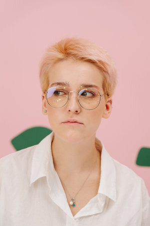 Sad sulking young woman with short dyed blond hair and round glasses and stars eye makeup. Over pink...