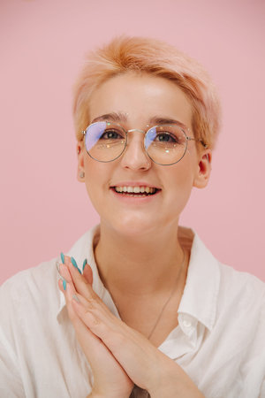 Cute smiling young woman with short dyed blond hair and round glasses and stars eye makeup. Over...