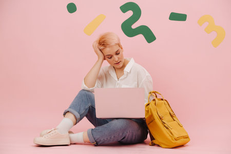 Young woman with short dyed blond hair sitting on the floor, working on a laptop. She wears mom...