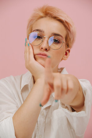 Extremely bored unsatisfied young woman leaning on her hand, pointing at you with her finger. She...