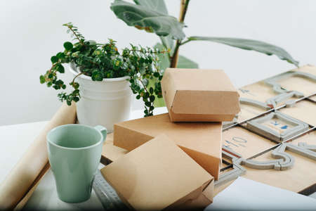 Messy workplace for designing and making cardboard boxes in a private workshop. Schematics, boxes, empty mug, potted plants and special board with a cutting form.の写真素材