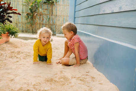 Outdoor summer portrait of two cute happy playing kids, big brother and his little sister against blue house wall. Girl is on all fours and boy is looking at her.の写真素材