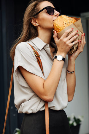 Happy mature business woman in sunglasses on the street, carrying crispy bread in her hands,...