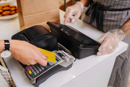 Woman making a purchaise, paying with her credit card. Baker standing behind cash register...