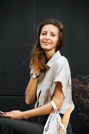 Happy mature woman in corporate clothing on the street. She's sitting on a planter box with bonsai...