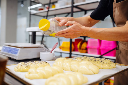 Male baker sprinkling raw uncooked bread with poppy seeds. Cropped, no head. Hands and body.