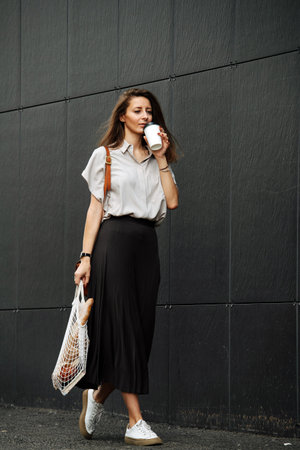 Casual mature business woman on the side of a street drinking coffee. She's wearing corporate...