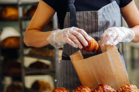 Baker placing freshly baked crispy golden croissants in a paper bag for delivery. Frontal viewの写真素材