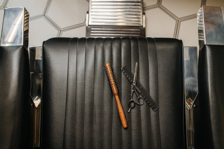 Top view image of round comb, classic straight comb and shears on a black hairdresser's chair.の写真素材