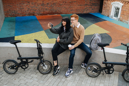 Smiling young couple sitting on a concrete border, taking selfie