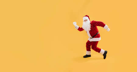 Santa cheerfully shows that he is running. He in a funny pose isolated on yellow background.の写真素材