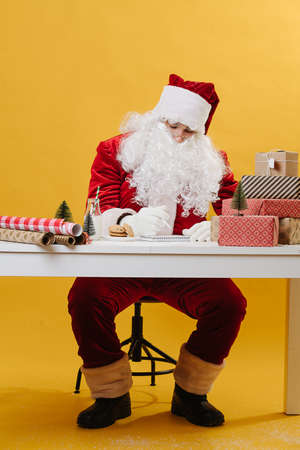 Santa Claus writes a letter at the table on a yellow background. High quality photoの写真素材