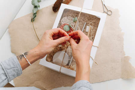 Woman hands tying windowed box with multi-use eco-friendly items. It also contains wooden brush, steel straw and woven makeup remover discs on a filling paper.の写真素材