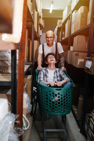 Silly warehouse workers having fun, man pushing cart with woman inside