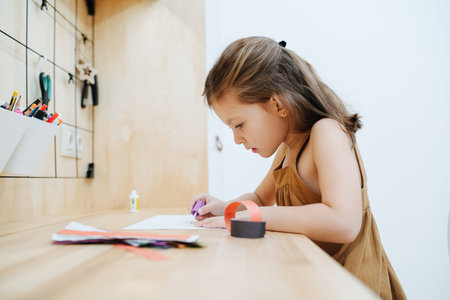 A 6-year-old girl sits at a table, she glues a garland of paperの写真素材