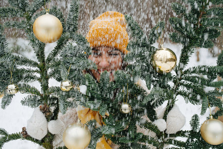 A girl stands behind a Christmas tree decorated with gold balls, blurred pictureの写真素材