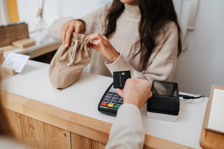 Shopkeeper putting goods in a fabric bag, woman hand paying with a cardの写真素材