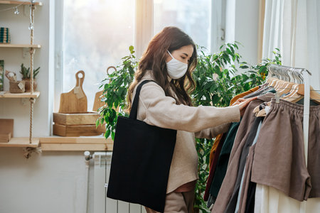 Masked woman in an eco shop looking through rack with synthetic-free clothesの写真素材