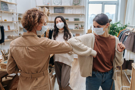 Two young women in an ecological shop greeting each other, touching elbowsの写真素材